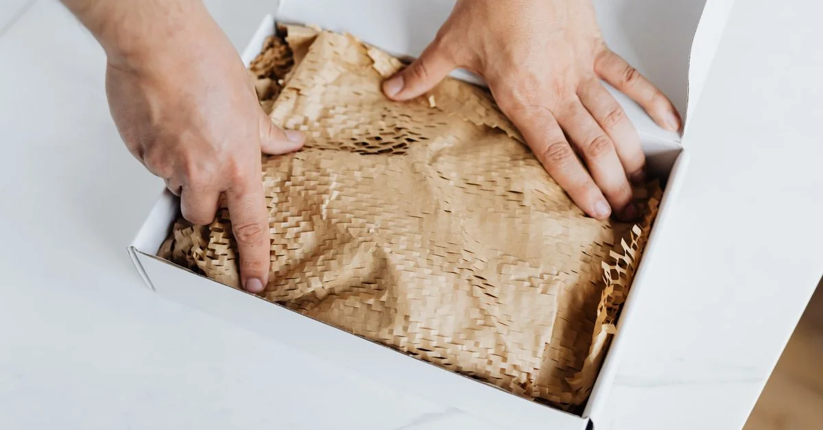 Gros plan sur des mains emballant une boîte en carton écologique avec du papier de protection, mettant en avant un emballage durable.