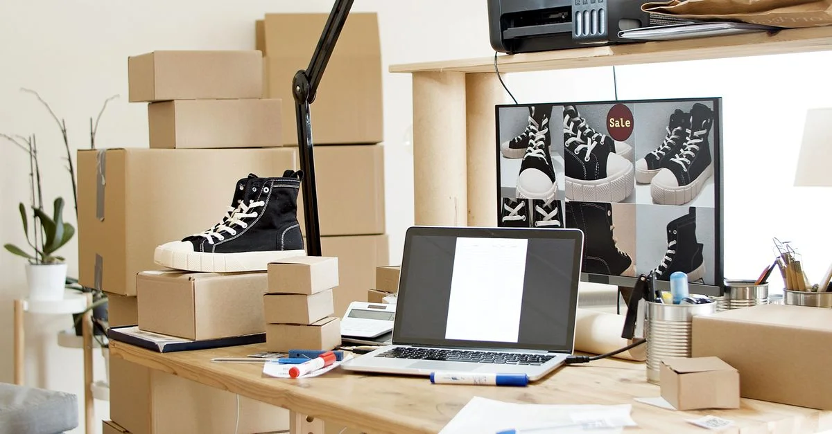 Un espace de travail occupé avec des baskets, des boîtes et un ordinateur portable indiquant un magasin de chaussures en ligne ou une configuration de commerce électronique.